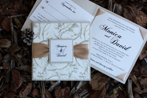 Square pyrite signature side pocket fold with ribbon and monogram tag, satin ribbon corners on invitation.