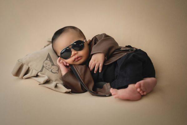 Newborn Baby boy posed on fabric backdrop with leather jacket and designer glasses