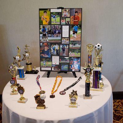 Hall set up a table and white tablecloth to Display Sport Trophies of Joshua's Achievements/ Accomplishments!  6/17/2023