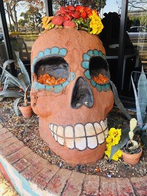 An enormous calavera sits in the planter by the main entrance.