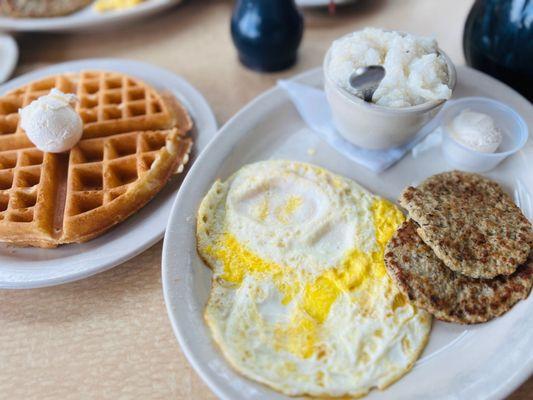 Hearty Breakfast with fully cooked over easy eggs, grits, chicken sausage, and a Belgian waffle