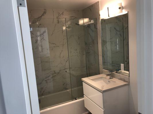 Two-piece frameless tub enclosure with one door and one fixed sidelite, mounted to tile with standard hinges and clamps. Mirror not provided