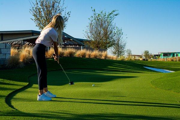 Female golfer practicing on Celebrity Greens synthetic turf putting course.