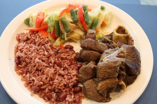 Curry Goat with Rice and Peas, Steamed Vegetables and Fried Plantains.