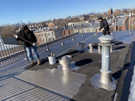 Installing reflective fibered aluminum roof coating on old flat roof. United roofing