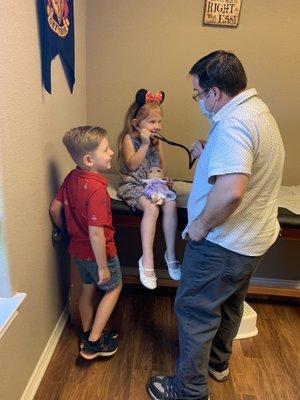 A patient and her brother smile as Dr. Holmes allows her to listen to his heart using his stethoscope