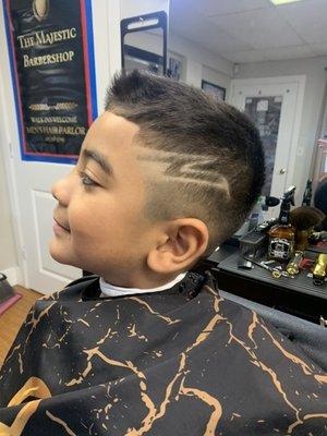 Thick wavy hair cut down to compliment this young boys face.  Mid-high fade, sharp front line-up and fun design for this cool kid look.