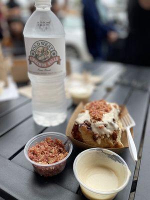 Old west contact cinnamon roll, bottle of water, side of maple frosting, side of bacon bits to sprinkle on top