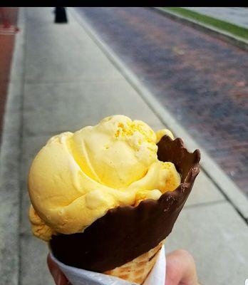 Two scoops of orange creamsicle in a chocolate waffle cone