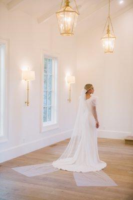 Aniston gown featuring a puff sleeve that tightens at forearm with beautiful buttons. Simple crepe fitted gown with a pearl bow veil.