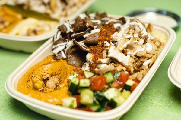 White rice bowl with chicken shawarma and gyro, sides of Spicy hummus and Mediterranean salad. dressed with chili sauce and garlic sauce.