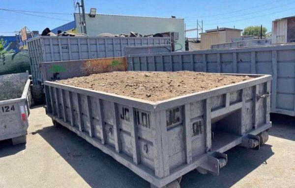 The lowboy container is a rectangular, heavy-duty dumpster with a low profile, typically around 16 feet long and 2 feet high.