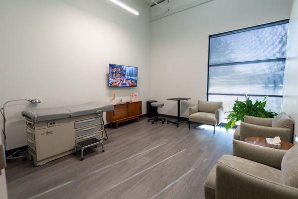 Exam room at Vertrae® with sofa chairs, large windows, and television