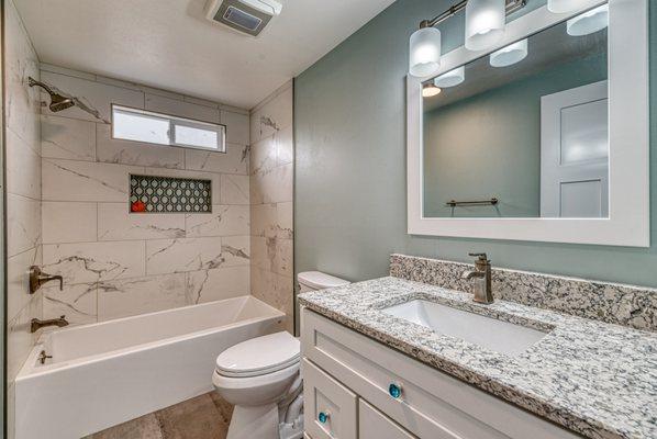 Fully remodeled guest bath. 12x24 wall tile with glass mosaic in niche for accent. New white shaker vanity and quartz countertop.