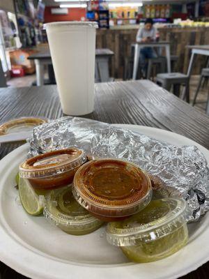 Wrapped carne asada burrito with red and green salsas and fresh limes