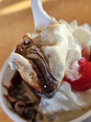 A spoonful of the ice cream sundae with soft vanilla ice cream and chocolate syrup.