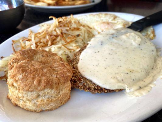 Chicken fried steak with eggs, hash browns and a biscuit.