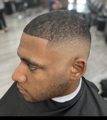 High skin fade with the top trimmed with the grain.  Clean boxed-out shape-up