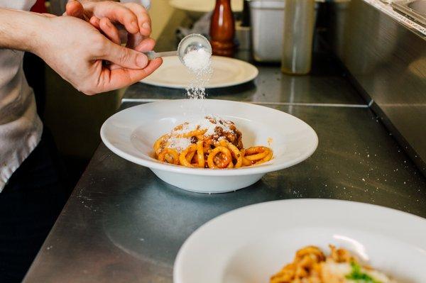 Chef decorating a bowl of Bucatini with Amatriciana sauce