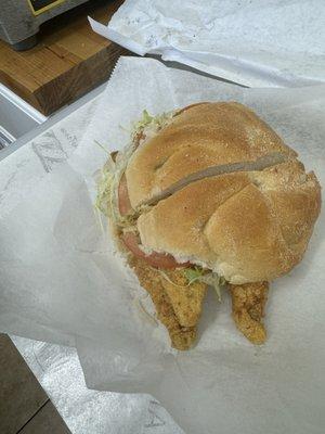 Fried fish sandwich on a roll with lettuce and tomato.