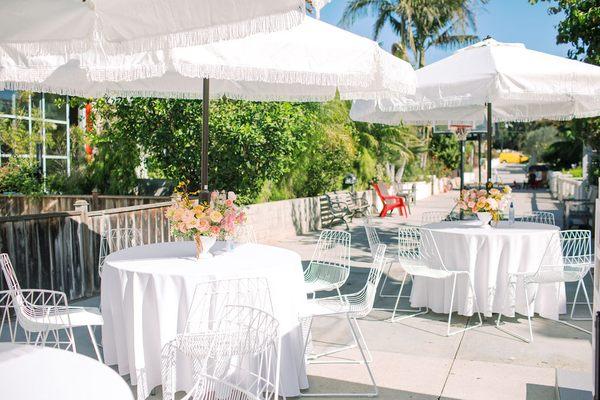 white fringe umbrellas, white wire chairs, 48" round tables