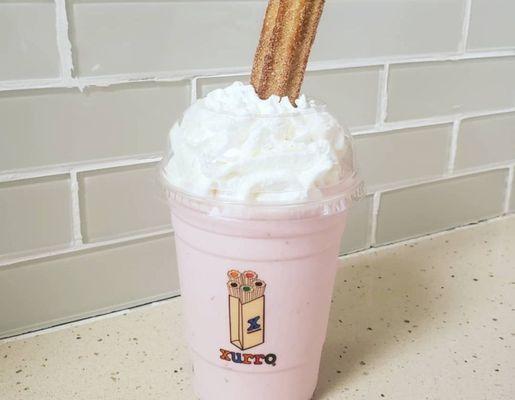 Strawberry churro milkshake with a whole churro dipped and whip cream.