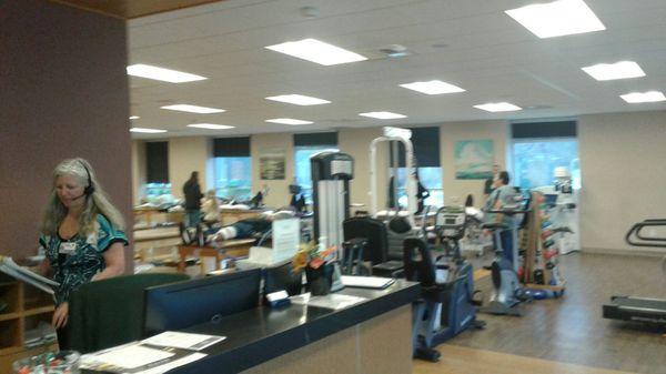 Exercise area with check in desk for Appointment sign in sheet and a clock. Clients on tables staff members assisting them.