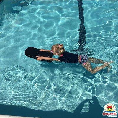 Kids swimming lessons - student practices her kick while holding a kick board