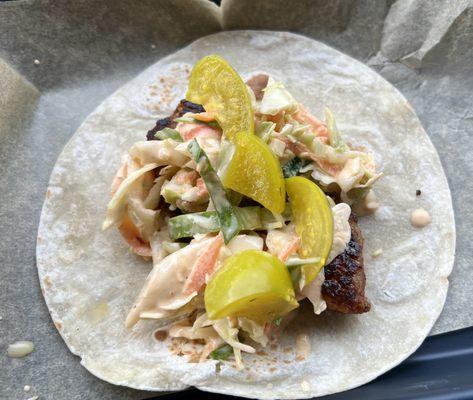 Pork belly taco with coke slaw and marinated tomatillos on a flour tortilla