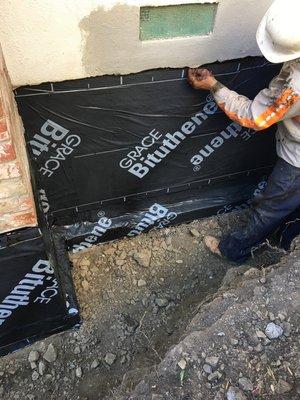 Here were applying a rubber membrane to waterproof the foundation before we install a French Drain.