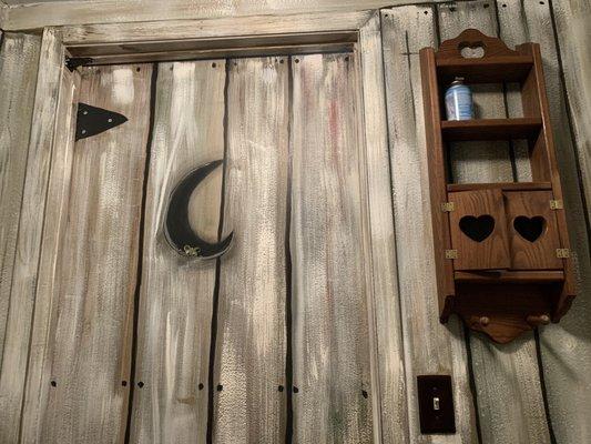 Inside of restroom painted like an outhouse. Zoom in to see little critter peeking in the crescent moon "window".