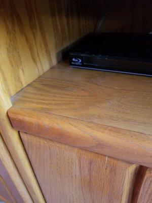 Entertainment center shelf by the DVD player, still with dust.