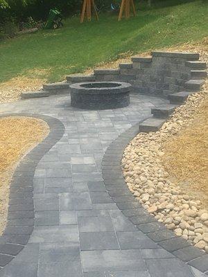 Sidewalk opens to a firepit surrounded by a beautiful retaining wall.