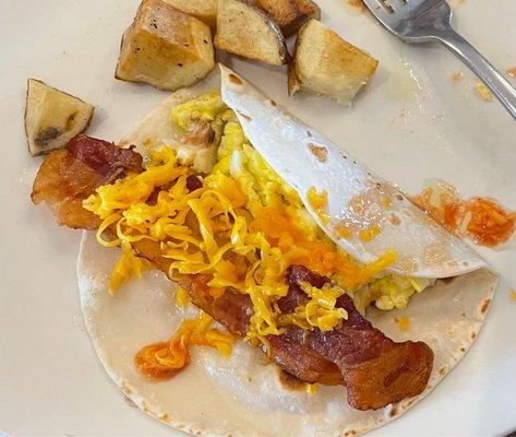 Breakfast taco of eggs, bacon and cheese. Potatoes are cubed.