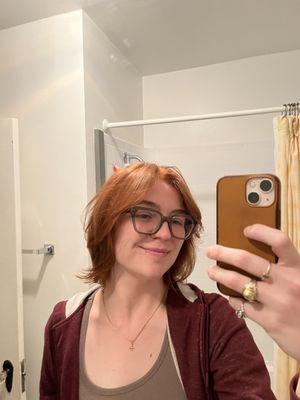 Woman smiles in front of mirror, showing red/orange haircut