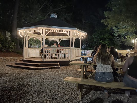 Outside gazebo. Gravel rocks. Seating is on a bench. Food and drinks are far away and you have to serve yourself.