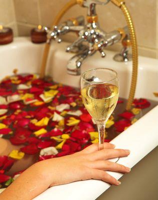 Empress Aromatherapy Bath, Woman in bath tub of rose petals and holding a glass of Champagne