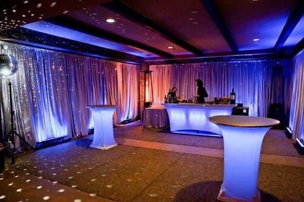 Luxury lounge featuring satin draped walls, up lighting, illuminated bar and cocktail tables. Who's ready for a drink?