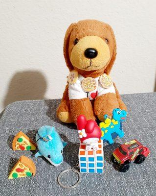 Aw, he got arcade prizes! Pizza erasers, little whale, keychains: dinosaur, mini Rubik's cube. Truck, and My Melody figurine.