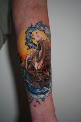 Capturing the grace of an elephant amidst a splash of water, this tattoo marries the majesty of wildlife with a burst of surreal artistry.