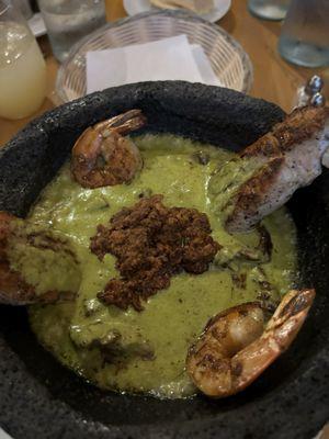 Molcajete (a bowl carved from volcanic rock) with chicken, shrimp, and skirt steak in a green chili cheese sauce.