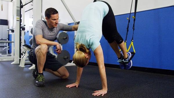 Personal Trainer George instructs a client while doing a TRX core exercise.