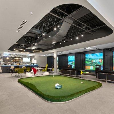 Our lobby area with a practice green, rest area and bar surrounded by driving range bays and course play bays.