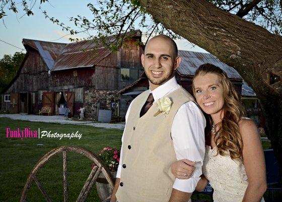 Groom and bride pose under the Wedding Tree in front of the Wedding Barn at the Civil War Ranch in Carthage, MO.