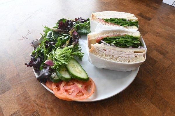 Turkey Sandwich: Turkey, Havarti, Spinach, Tomato, Red Onion, Aioli on Sourdough Bread.  Accompanied by a side salad.