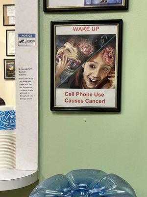 A sign in the waiting room that says "WAKE UP Cell Phone Use Causes Cancer!"