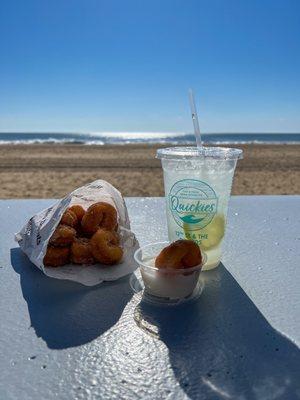 Half eaten bag of donuts, vanilla dipping sauce, and lemonade