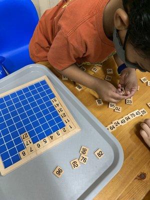 A child working with the hundreds board. He was figuring how the unit stays the same and the tens changes in each row.