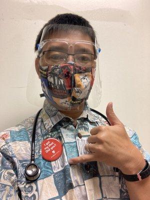 Dr. Brent Tamamoto flashes a shaka while showing off his Personal Protective Equipment and COVID-19 shot button.