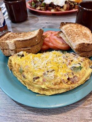 Kitchen Sink omelette with wheat toast and sliced tomatoes.